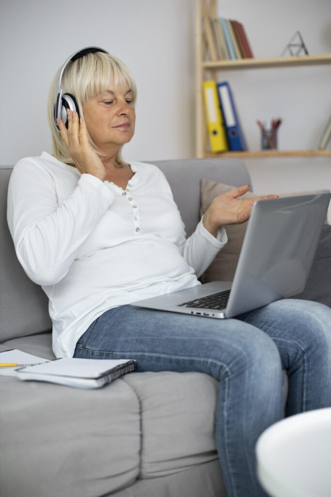 Femme en séance d’hypnose en visio, assise chez elle avec un casque, en conversation avec son hypnothérapeute sur l’écran de son ordinateur, pour illustrer le déroulement d’une séance d’hypnose à distance.