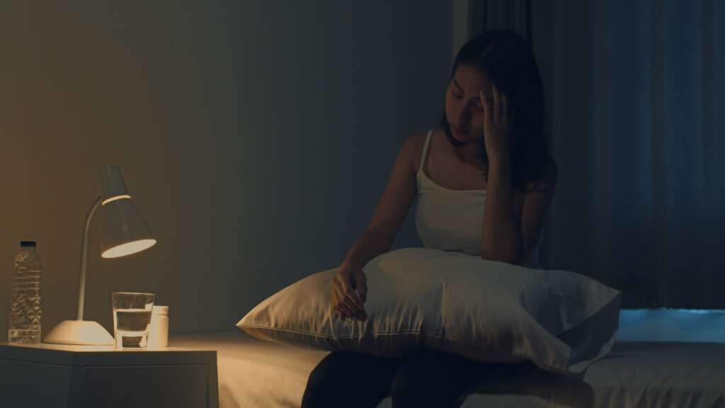 Femme souffrant d'insomnie assise sur son lit dans le noir, la tête dans la main