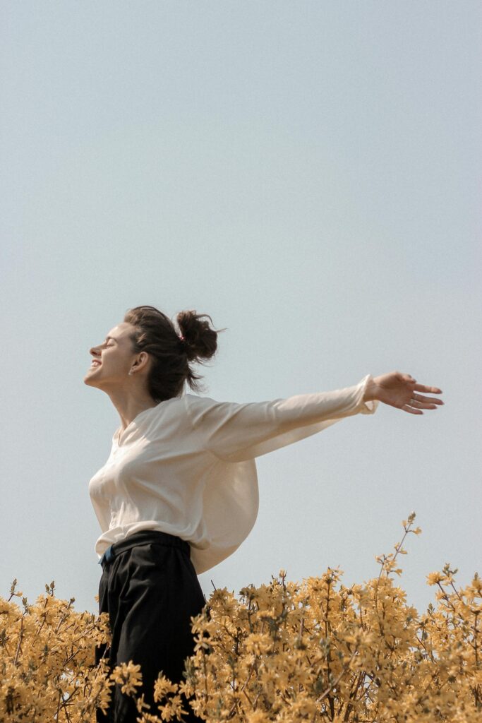 A woman in a white blouse enjoys the outdoors in a springtime field of yellow flowers.
